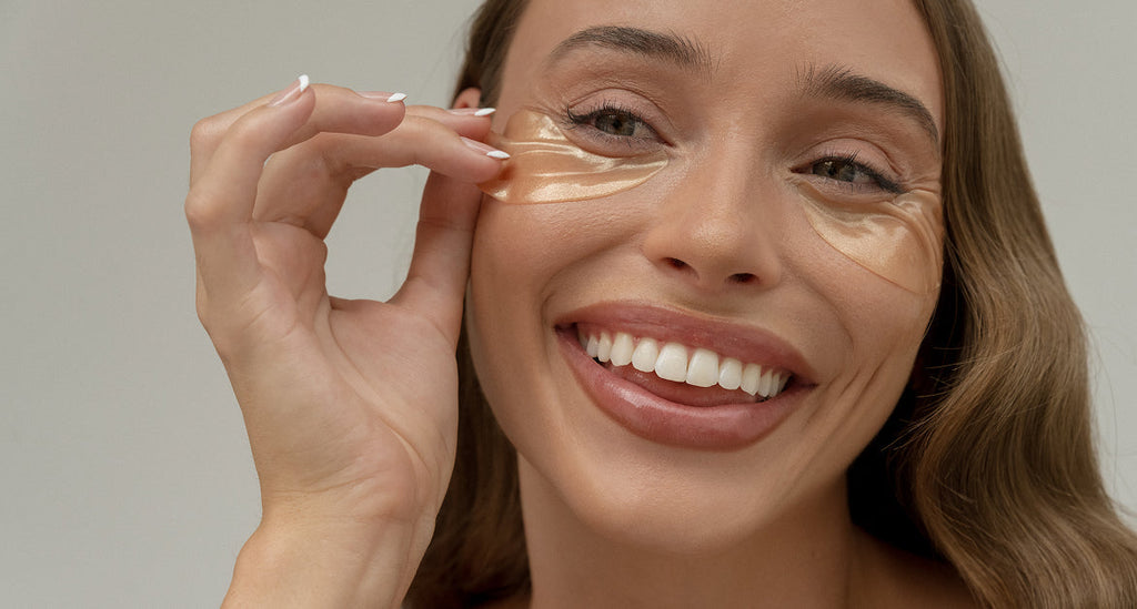 Smiling woman applying a gold GINGER&ME Hydra Glow Eye Mask under her eye.